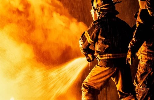 Two firefighters fighting a fire with a hose and water