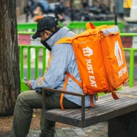 man in gray and orange jacket and black pants sitting on brown wooden bench