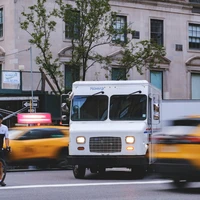 Man on unicycle rides past delivery truck and taxis