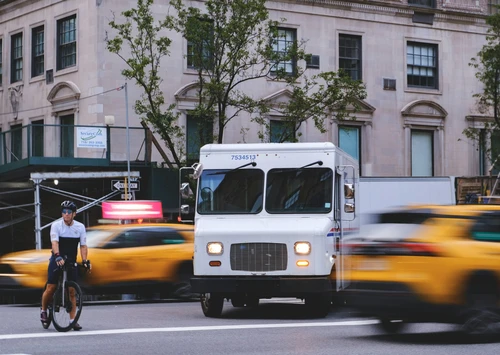 Man on unicycle rides past delivery truck and taxis