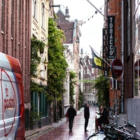 People walk down a narrow street with bicycles.