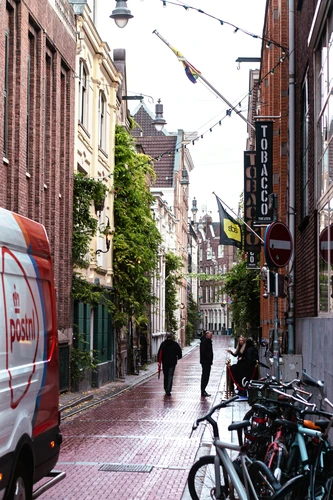 People walk down a narrow street with bicycles.