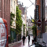 People walk down a narrow street with bicycles.